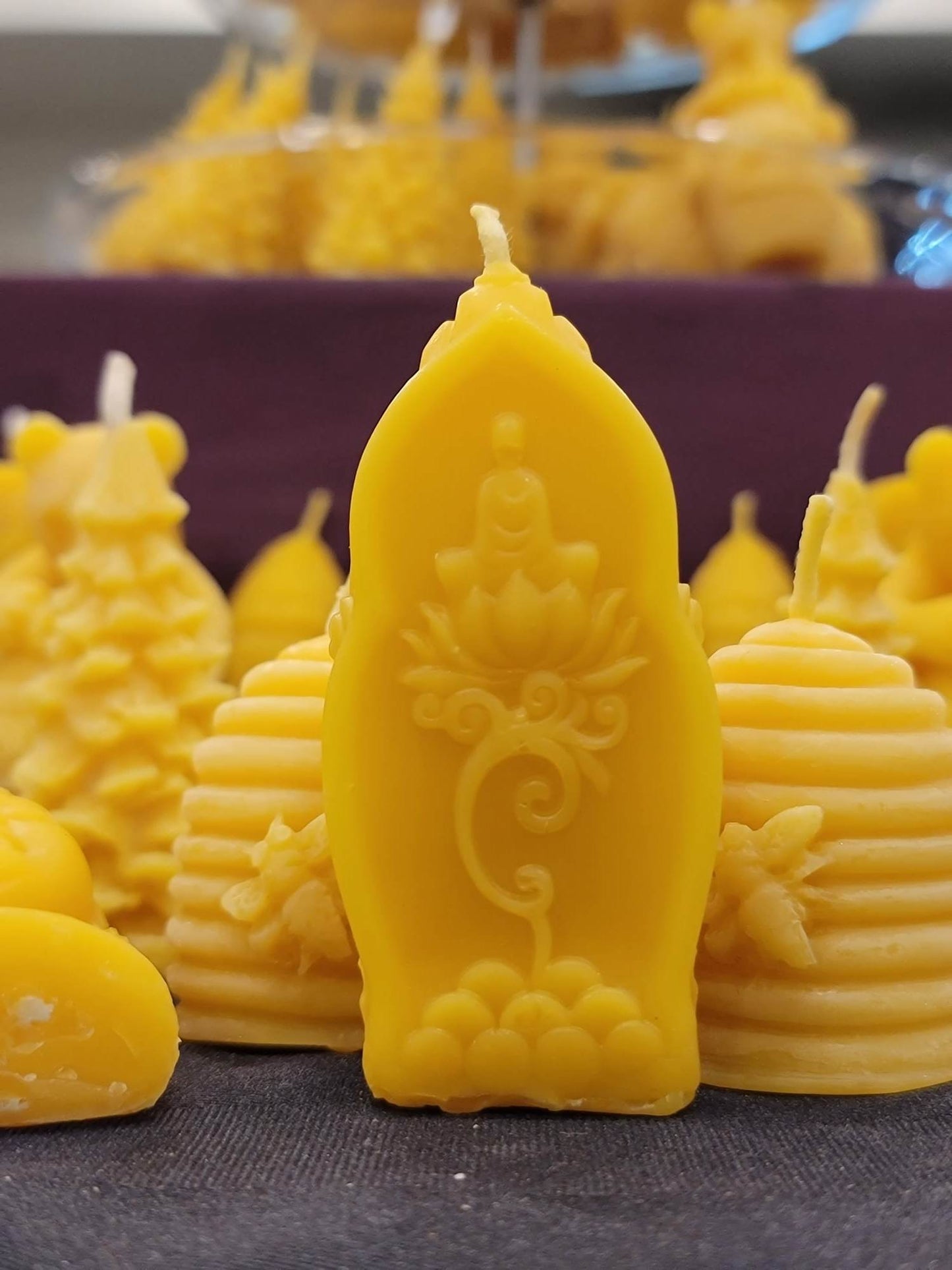 Une chandelle jaune au design de fleur de lotus devant plusieurs autres modèles de chandelles jaunes.