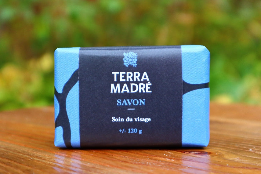 Savon pour le visage de 120 gr et son emballage bleu déposé sur une table dans le jardin