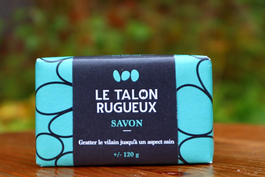 Savon exfoliant de 120 gr et son emballage bleu-turquoise déposé sur une table dans le jardin