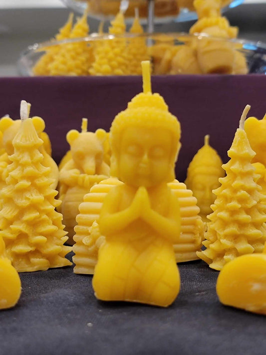 Une chandelle jaune en forme de bouddah agenouillé devant plusieurs autres modèles de chandelles jaunes