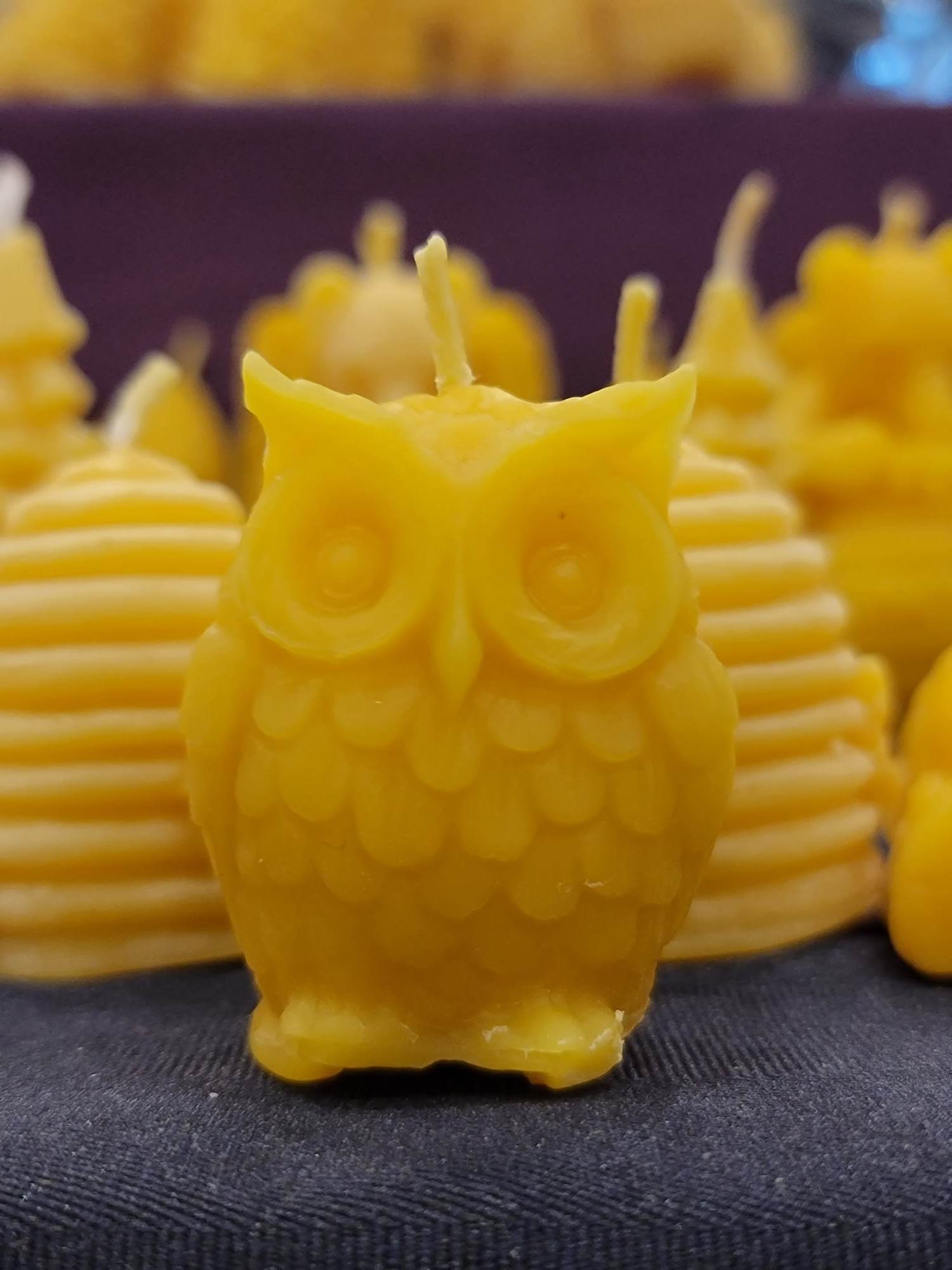 Une chandelle jaune en forme de hibou devant plusieurs autres modèles de chandelles jaunes.