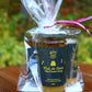 Emballage cadeau d'aromiel et de miel avec un ruban rose déposé sur une table dans le jardin.