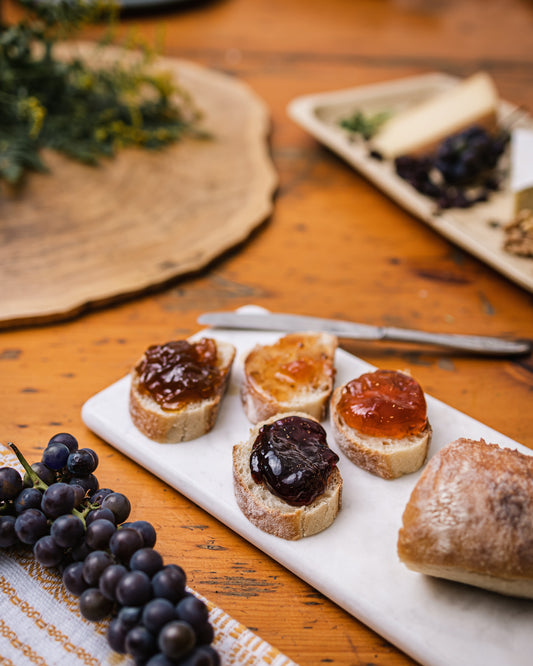 Une assiette de craquelin tartiner de différents confits, gelées et tartines sur une table de bois et entourer de raisins noirs.