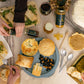 Table rempli de petit plats tel que des quiches, tartes, fromage, miel, noix et ustensiles