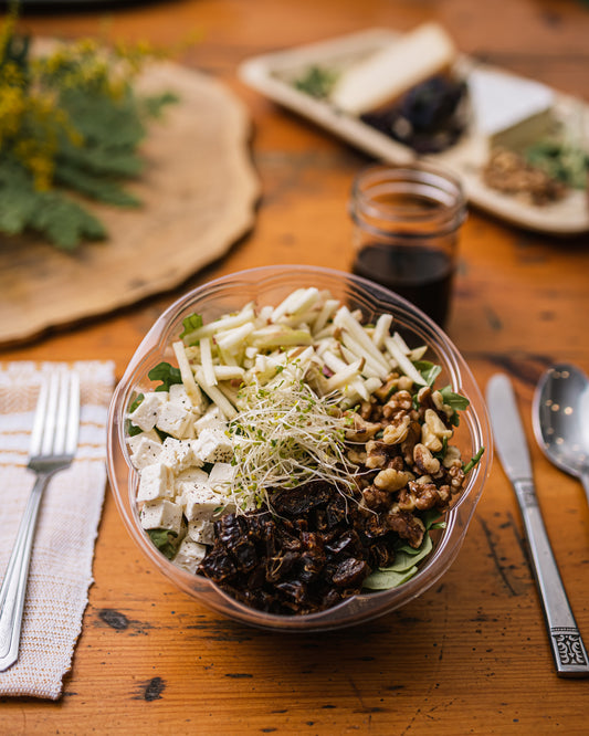 Une assiette de salade composée de roquettes, pommes, noix et dattes sur une table en bois