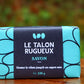 Savon exfoliant de 120 gr et son emballage bleu-turquoise déposé sur une table dans le jardin